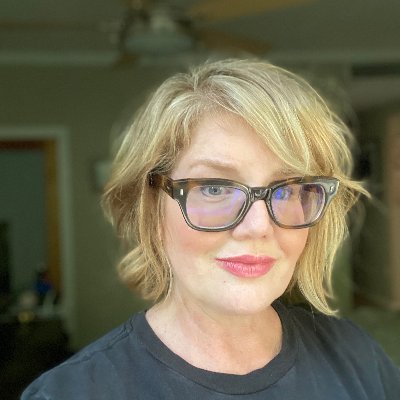 Image of a woman with short blond hair wearing glasses and a dark gray shirt. 