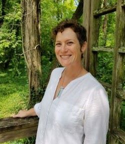 woman in a white blouse with tree and greenery in the background