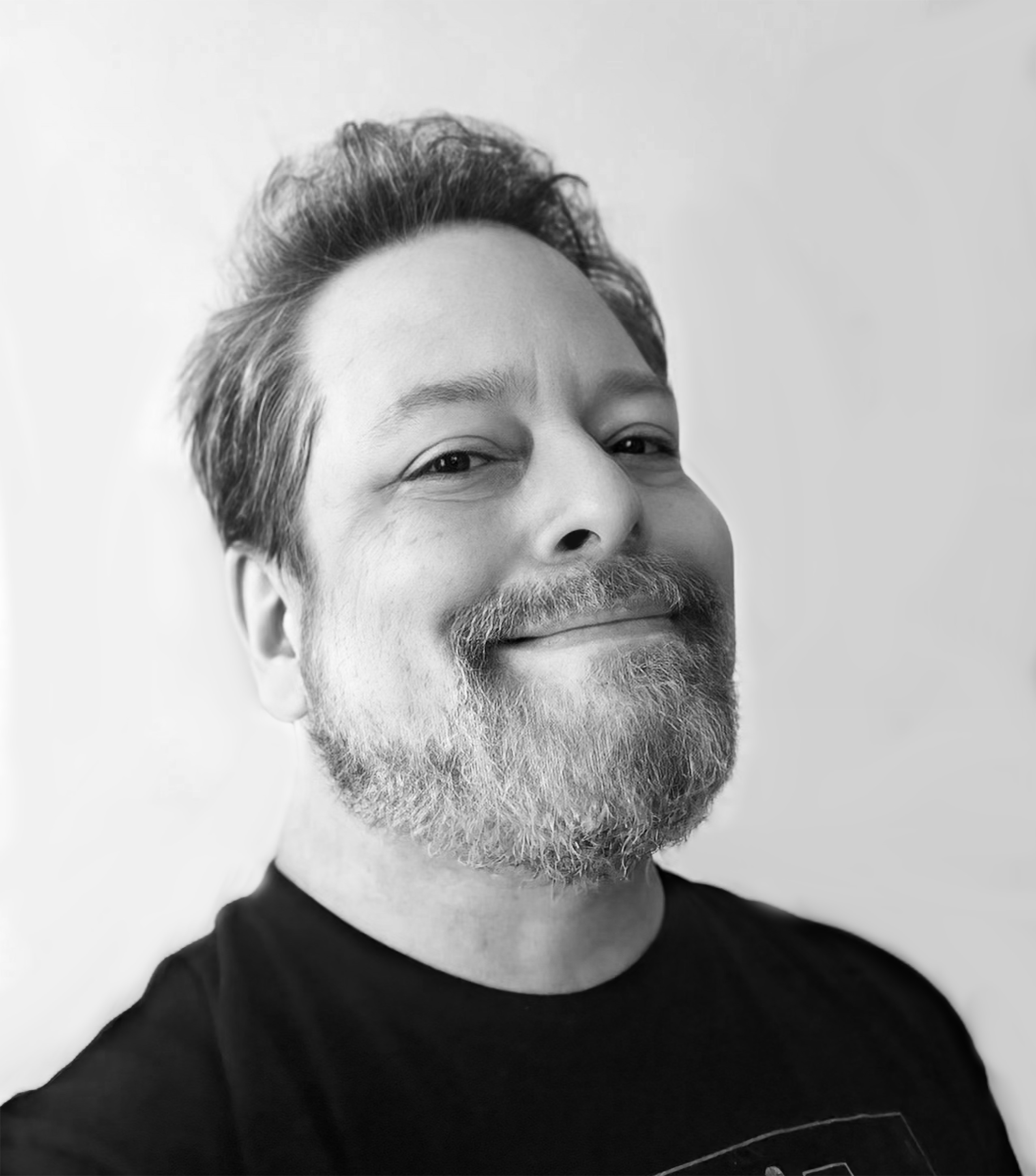 Black and white image of a smiling man with a short beard wearing a black shirt.