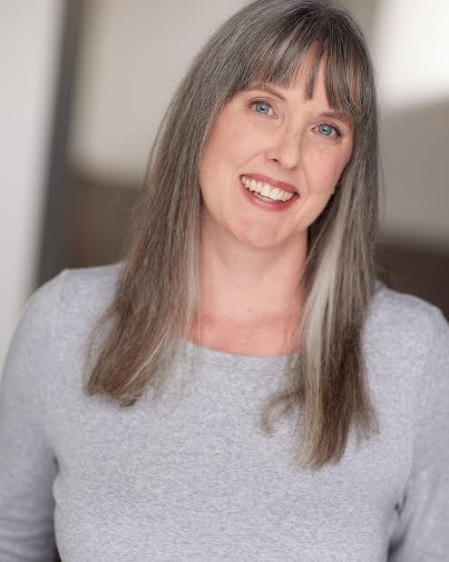 Image of a woman with blue eyes wearing a grey shirt and smiling at the camera.
