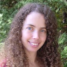 Image of a smiling woman with blue eyes and very curly brown hair. Behind her are leaves.