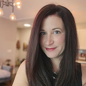 Image of a white woman with dark brown hair that has some red tint to it. She has blue/grey eyes and is smiling at the camera.