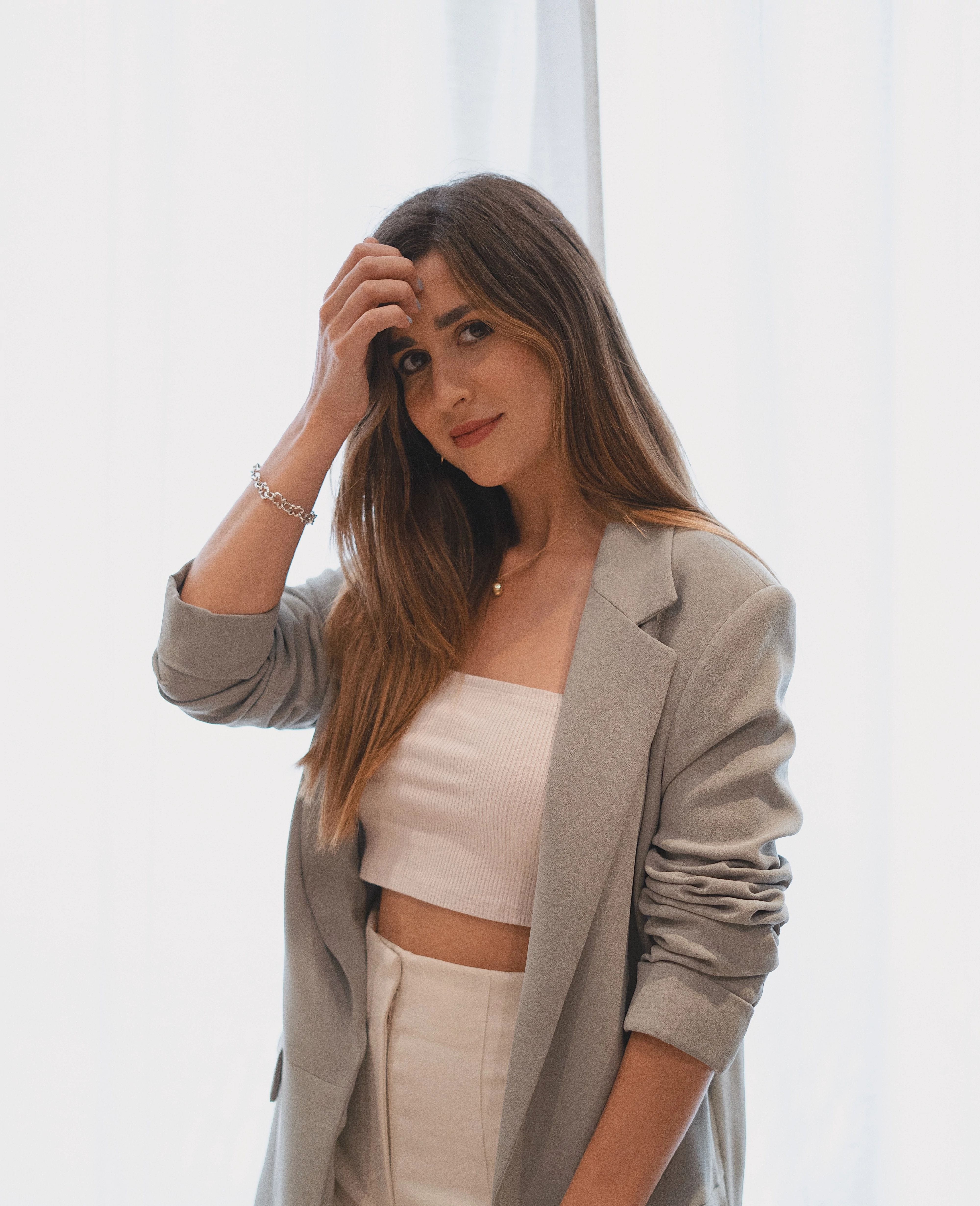 Image of a woman with long brown hair wearing a white shirt and pants with a grey jacket over it. 