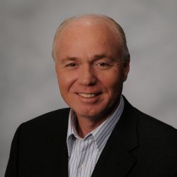 headshot of an older gentleman in a black suitcoat with grey background