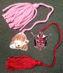 A charm bookmark of Tohru Honda with a pink tassel, and a Gundam charm bookmark with a red tassel