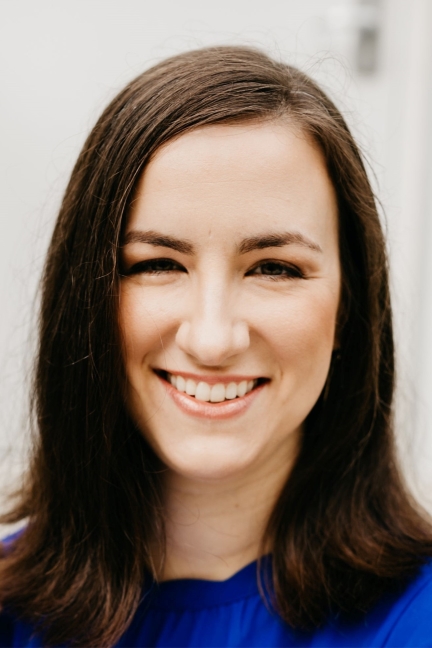 Image of a white woman with long dark brown hair, wearing a bright blue shirt. 