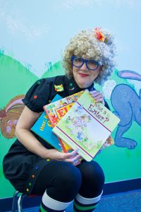 Reading Rita - A woman in a blonde wig and glasses showcases some picture books. 