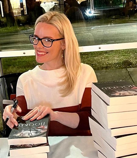 Image of a blond woman sitting at a table signing books