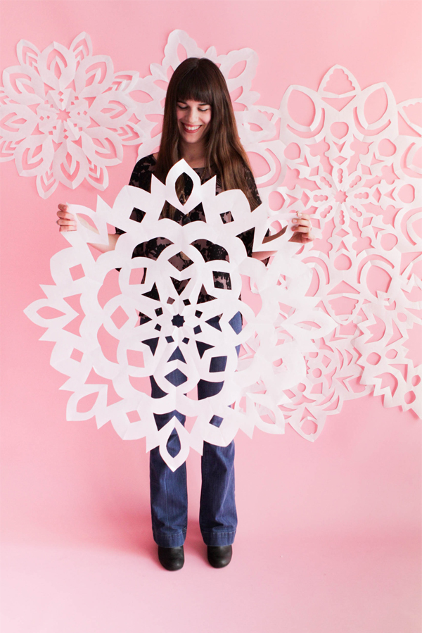 a woman holding a large white paper snowflake with more snowflakes in the background