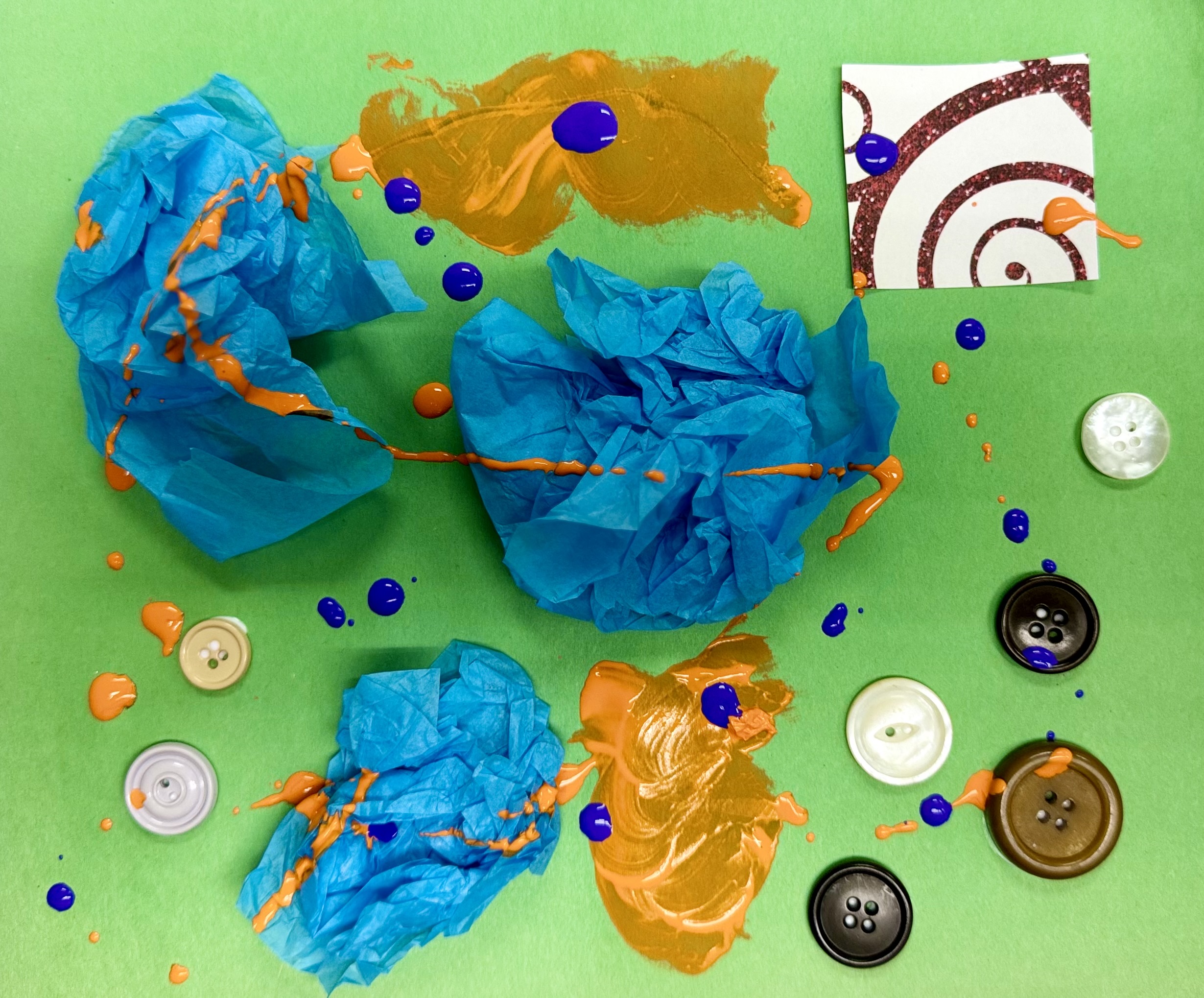 Green paper decorated with blue tissue paper, buttons, and purple and orange paint