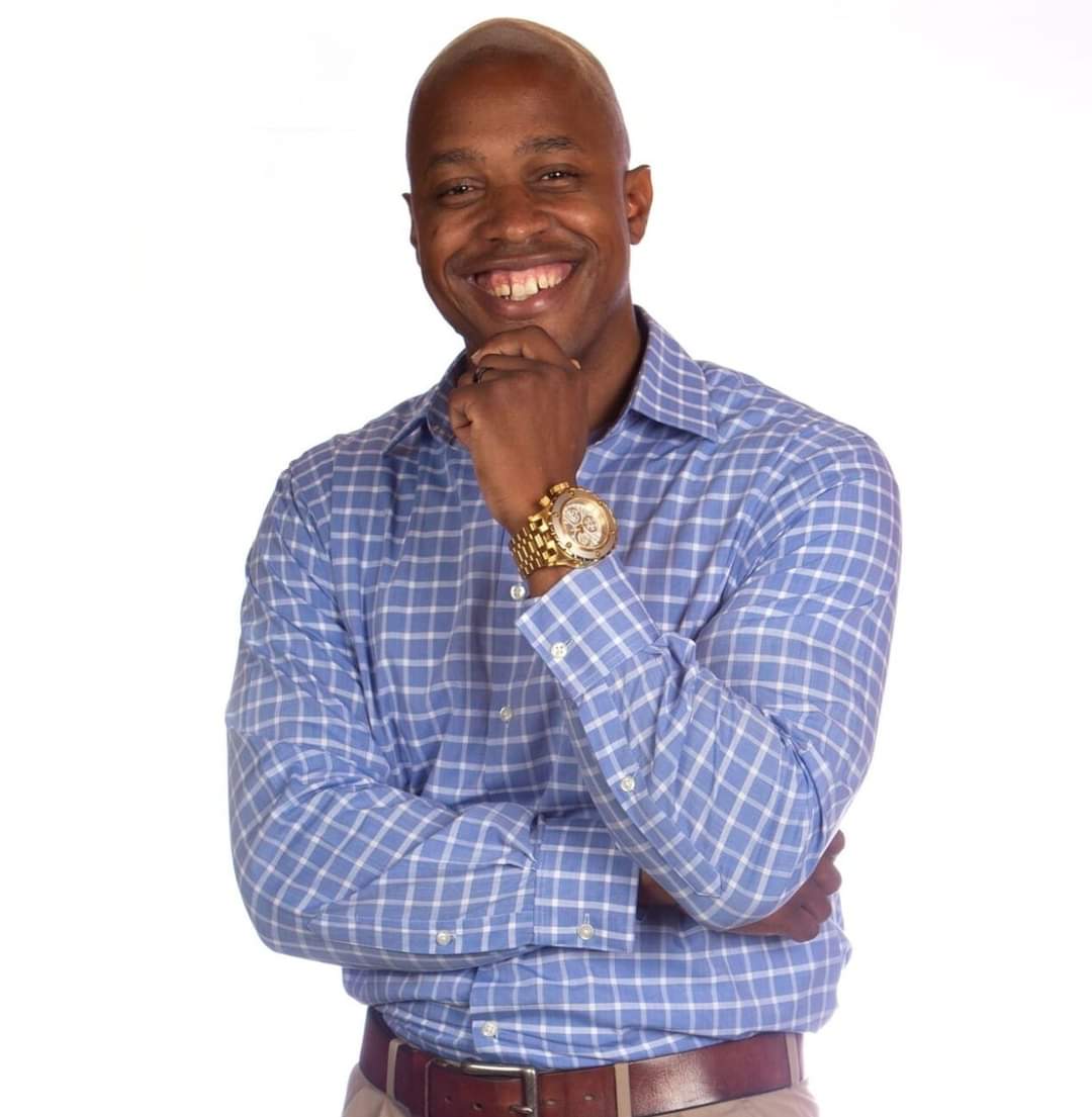 Image of a smiling African American man in a blue and white plaid shirt.