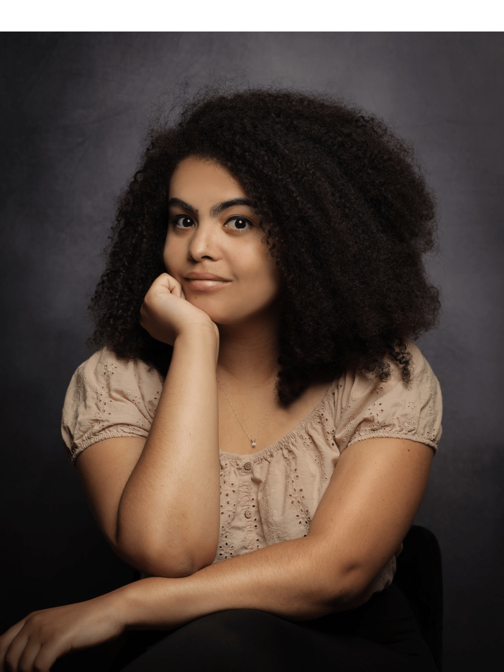 A woman with curly black hair sits in front of a grey background