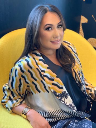 A woman smiles at the camera while sitting in a yellow chair.