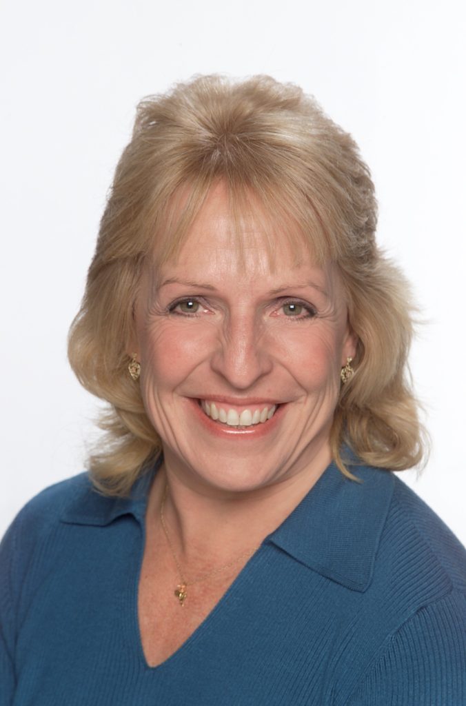 Image of a smiling woman with blond hair wearing a blue shirt. 