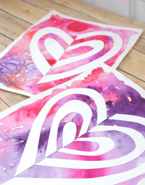 Image showing an art project made with a purple and pink watercolor background and silhouettes of white paper hearts.