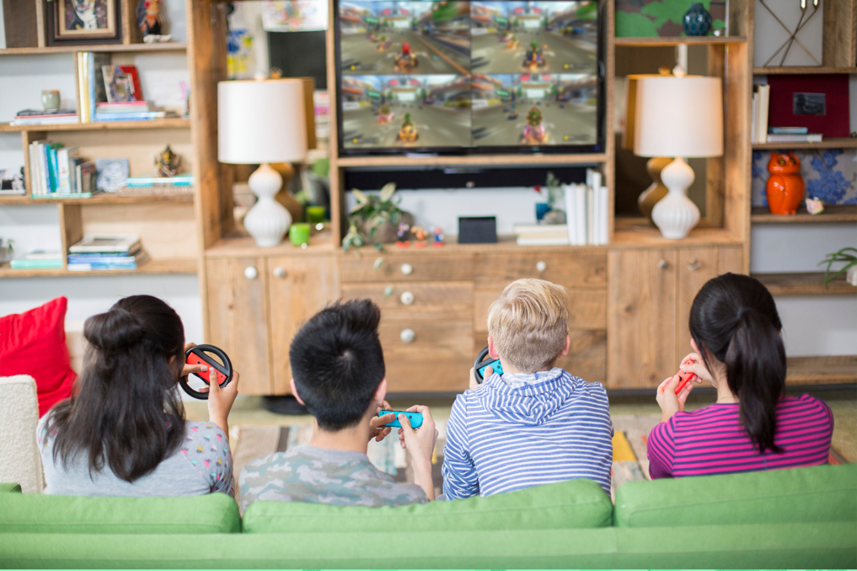 4 teens sit in a row in front of TV playing video game. 