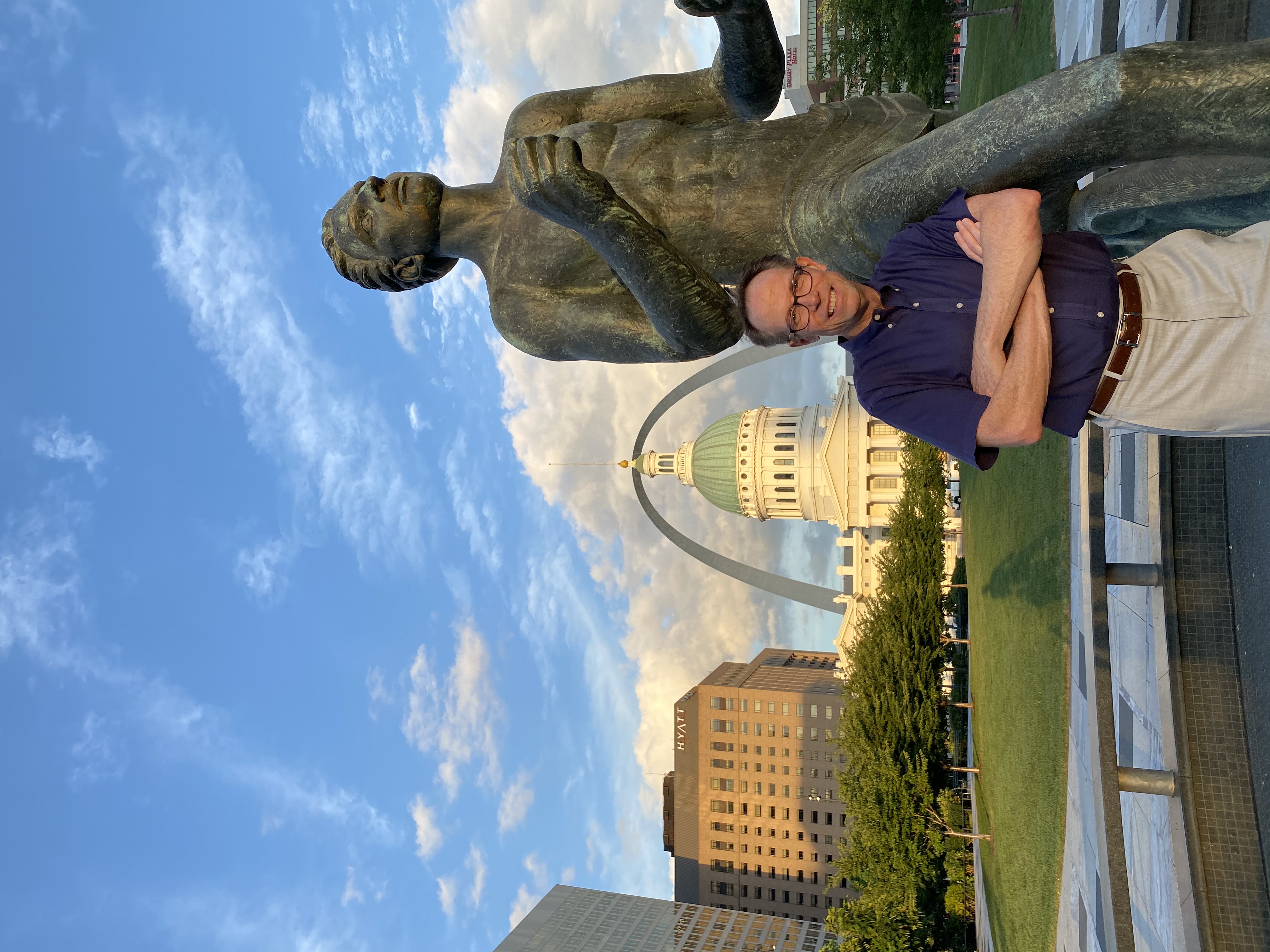 Image of Charlie Brennan standing next to the Running Man statue with the St. Louis Arch and the Old Courthouse in the background.