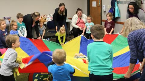 Group of preschoolers and adults playing with a parachute