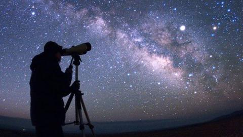 Person looking through a telescope at a starry night sky
