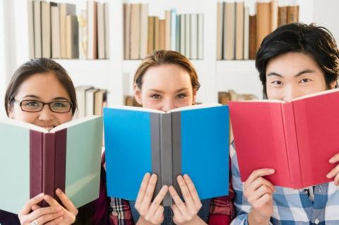 Three teenagers holding open books in front of them.