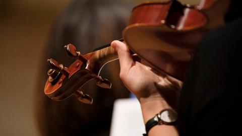 An up close image of a hand holding a violin, ready to play. 