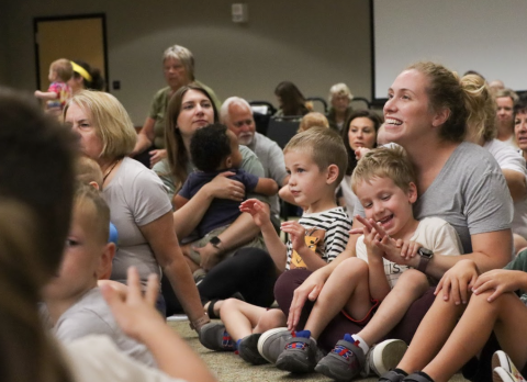 Kids and parents sit on the floor listening to a presentation