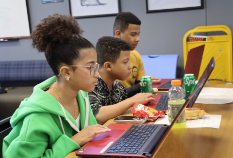 Three teens use laptops to study, each has snacks and drinks
