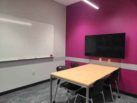 Study room with a table and chairs. There is a white board on one wall and a tv mounted on another wall. 