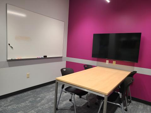 Study room with a table and chairs. There is a white board on one wall and a tv mounted on another wall. 
