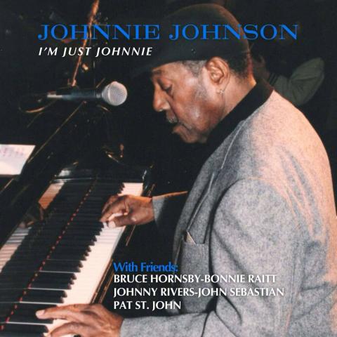 Image of a man playing piano and singing into a microphone. The man is African American, wearing a grey suit and a black hat.