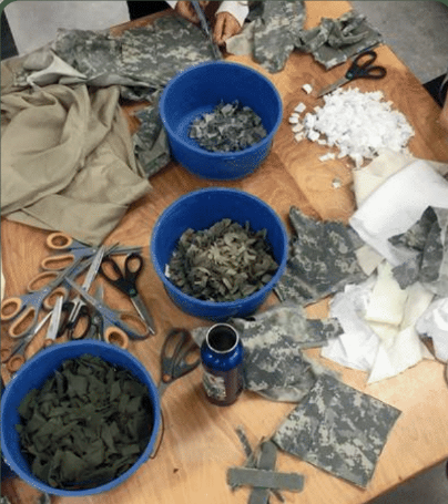 A table covered with United States military uniforms, scissors, and bowls with pieces of the uniforms. 