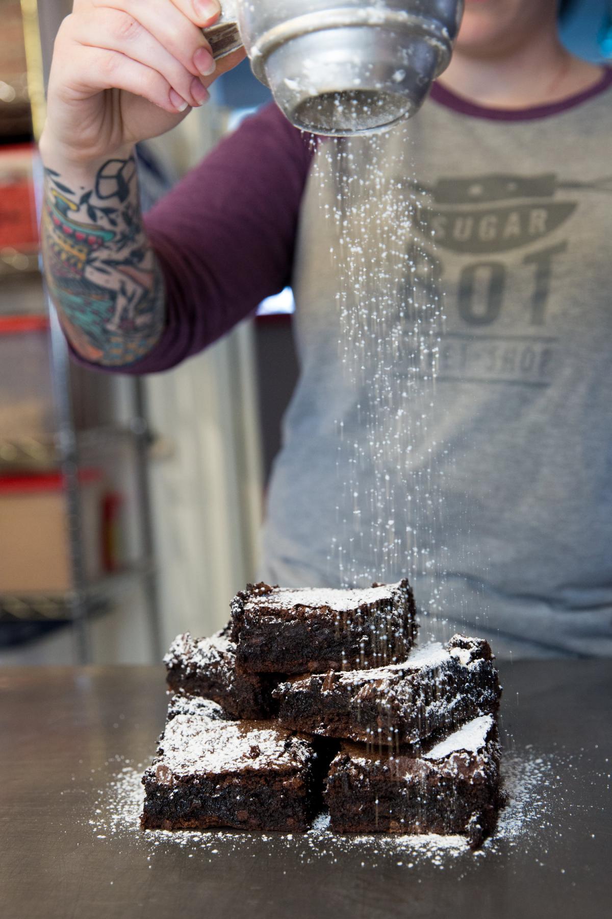 SugarBot staff member sprinkling powdered sugar on a stack of brownies. 