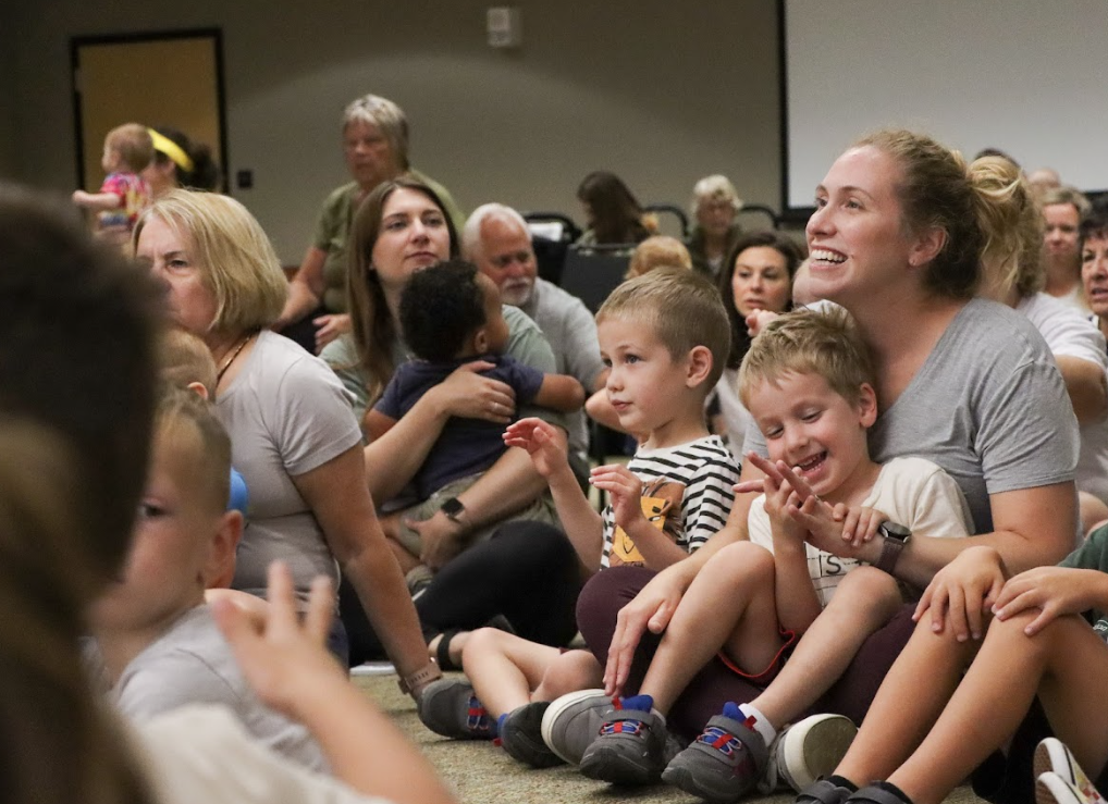 Kids and parents sit on the floor listening to a presentation