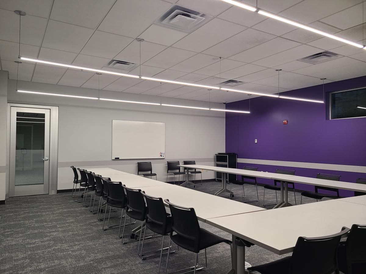 Meeting room with a purple wall, and tables and chairs set up in a horseshoe shape.