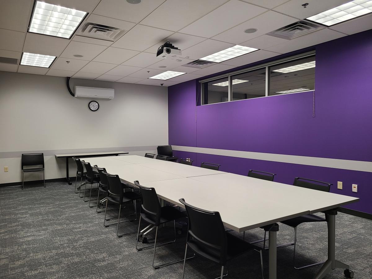 Long thin conference room with a purple wall and long table with chairs.